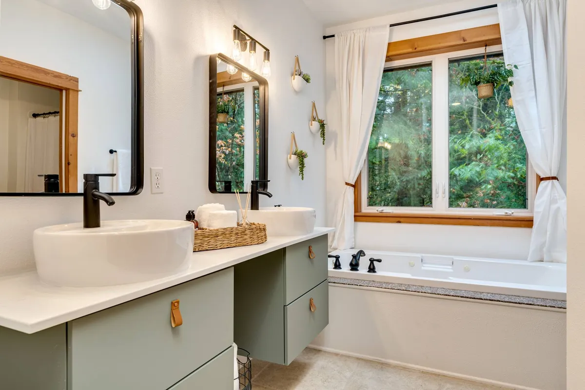 A spa-like bathroom interior featuring a large bathtub, modern double sinks, and a big window overlooking lush greenery. Gentle natural light streams in, creating a serene and inviting atmosphere ideal for relaxation and shared moments.
