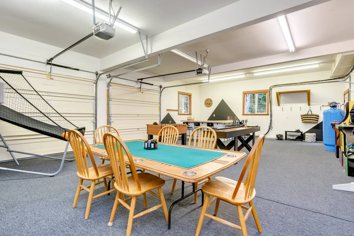 A versatile entertainment room featuring a game table with green felt, a ping pong table, sliding doors providing natural light, and a casual seating arrangement. The space is spacious and designed for group play and celebrations.