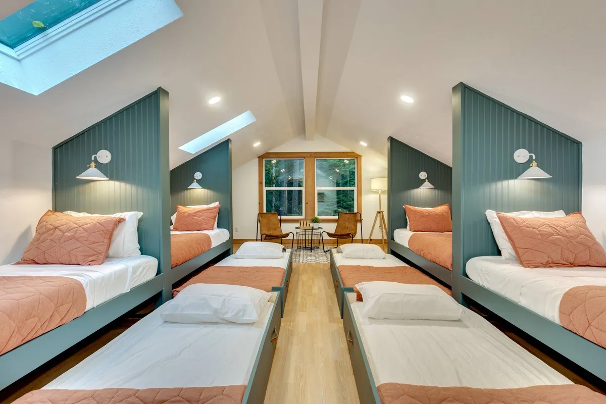 A playful custom bunk room with multiple bunk beds, a large window for natural light, and a cozy sitting area. The beds each have their own reading lights, creating a perfect sleepover environment for kids and groups.