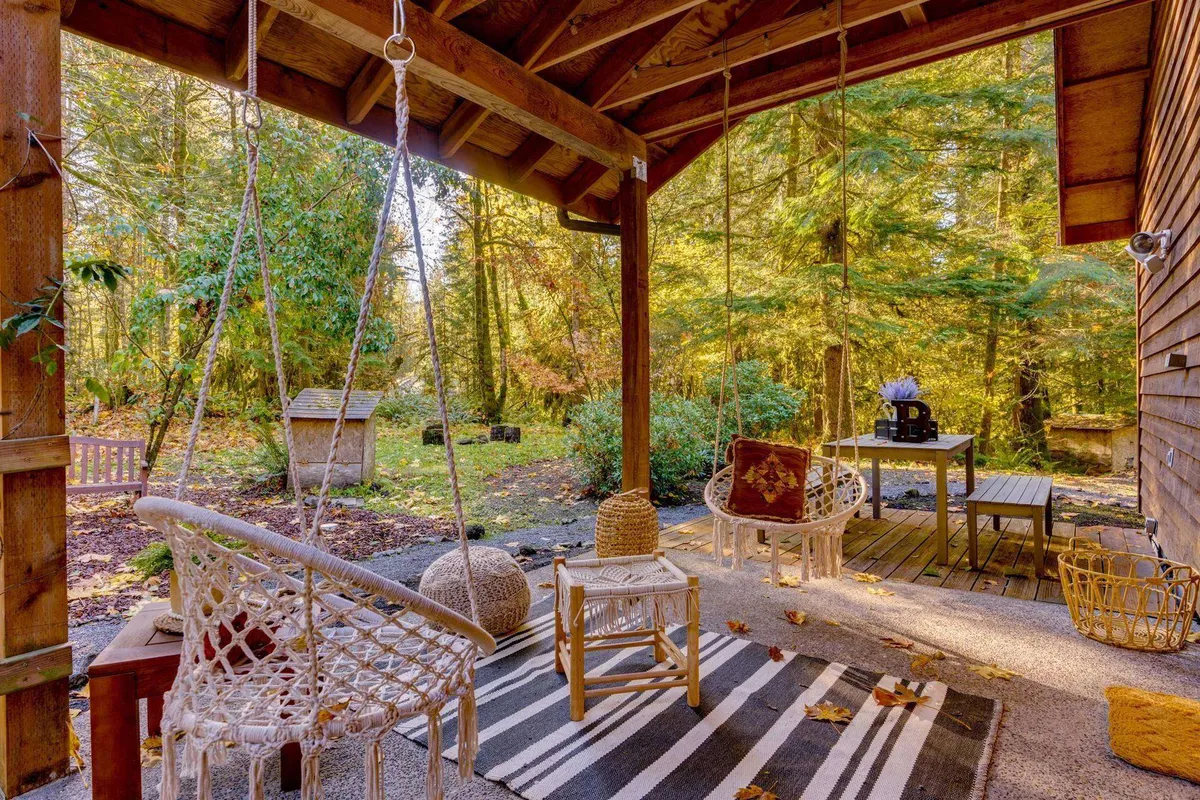 A tranquil wooden deck features hanging egg chairs and a small decorative table, all overlooking a forested backdrop. The setting invites relaxation, reading, and enjoying fresh air in a quiet, private environment.