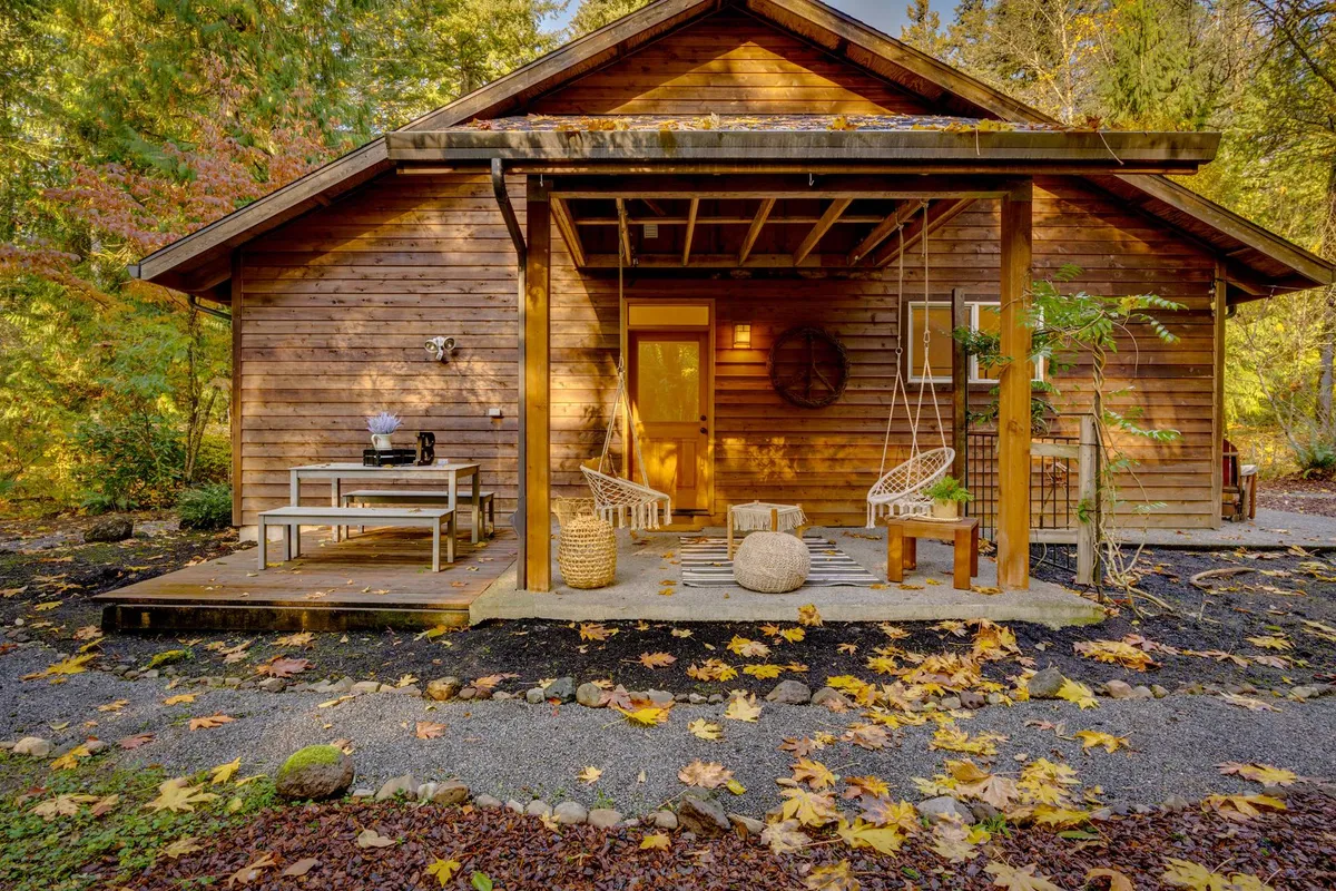 A welcoming wooden porch with cozy swing chairs and a decorative wall piece, set against a backdrop of autumn leaves. The outdoor seating area invites quiet reading, morning coffee, or friendly conversations, all in a peaceful, nature-filled environment.