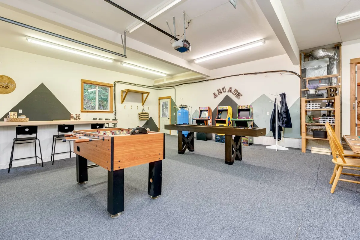 A cozy yet energetic playroom with a foosball table, arcade games lining the wall, a bar area, and a wooden table for socializing. The design is inviting to both adults and children, encouraging casual hangouts and friendly competition.